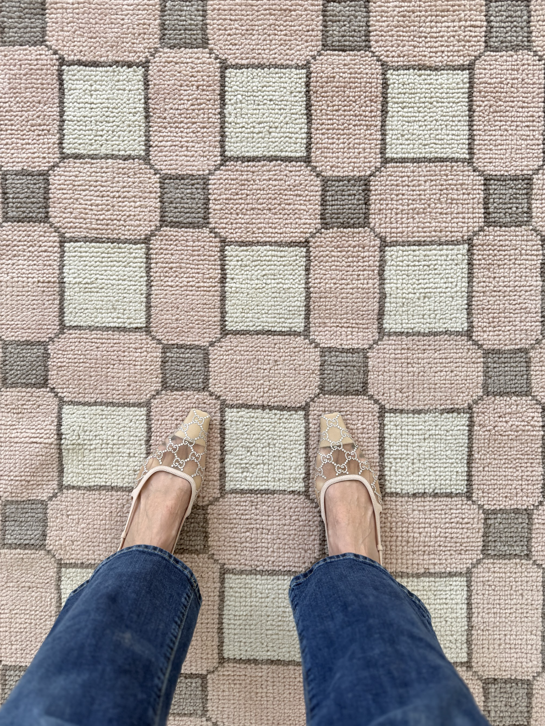 Person wearing blue jeans and beige shoes standing on a patterned carpet