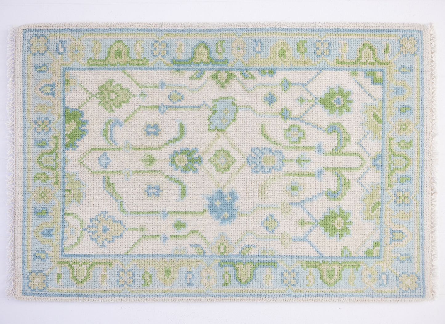 Emogene Mini Rug featuring a vintage-inspired Oushak pattern in soft blue, green, and ivory tones with decorative fringe.
