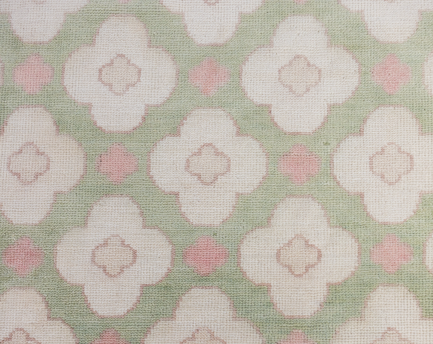 Pattern of white flowers with pink centers on a green background on a handknotted rug