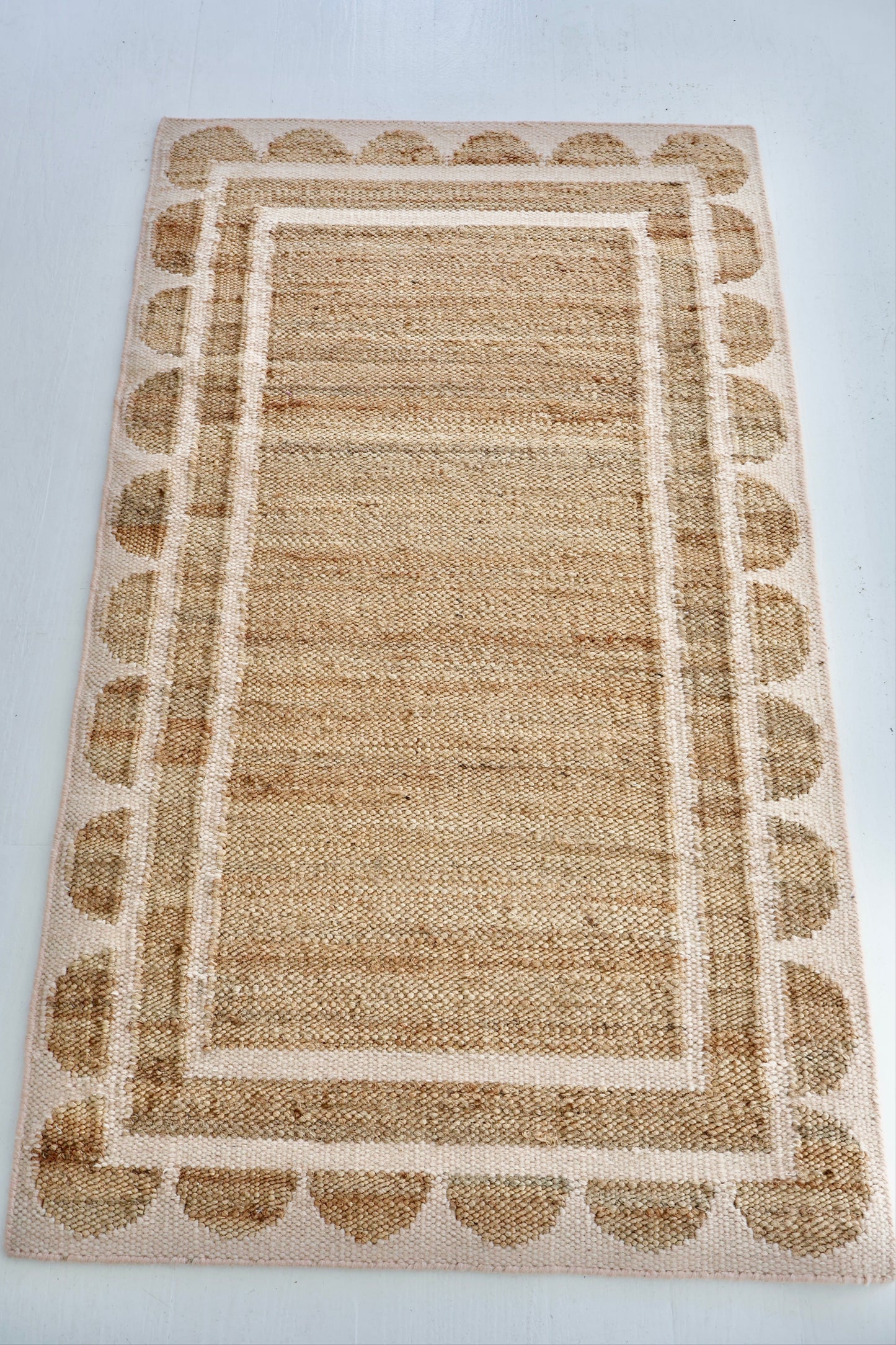 Handwoven jute and wool rug in natural tones with a soft blush pink scalloped edge border – Pink Palm Scalloped Edge Rug by Locust Lane Rugs