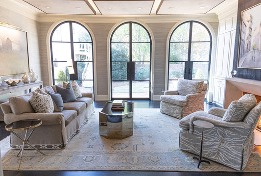 Bright living room featuring a handcrafted Modern Oushak wool rug in soft blue, ivory, and warm neutral tones beneath arched windows.
