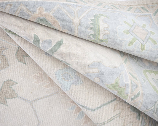 Folded hand-knotted wool rug with soft blue, sage green, and ivory geometric Oushak pattern