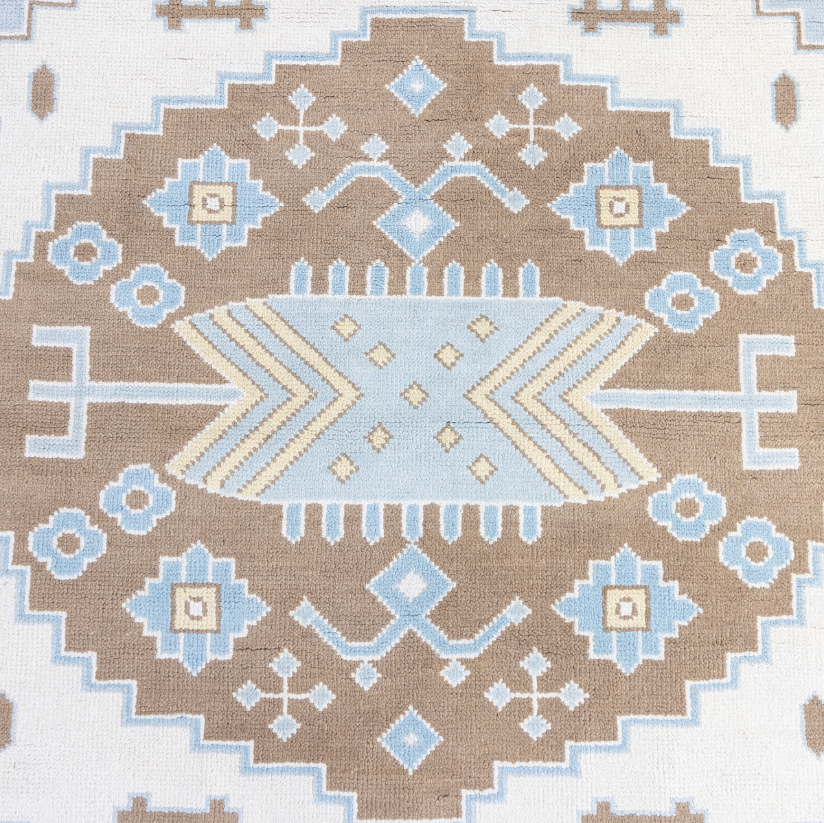 A close-up of a woven rug featuring a geometric medallion pattern in brown, light blue, cream, and white.