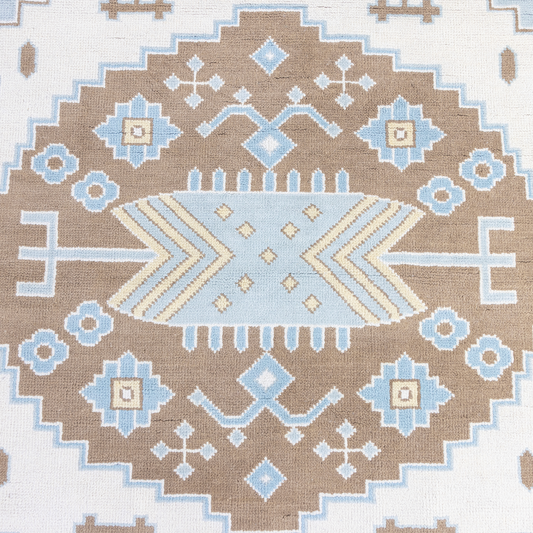 A close-up of a woven rug featuring a geometric medallion pattern in brown, light blue, cream, and white.
