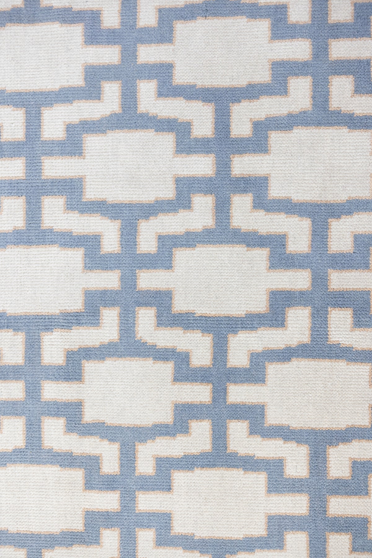 A close-up of a woven rug with a repeating geometric lattice pattern in light blue and off-white.