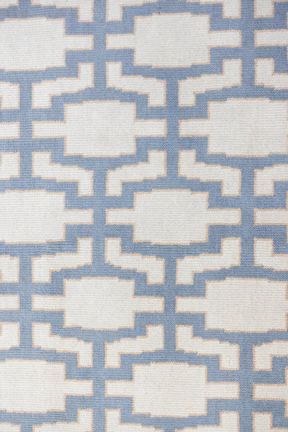 A close-up of a woven rug with a repeating geometric lattice pattern in light blue and off-white.