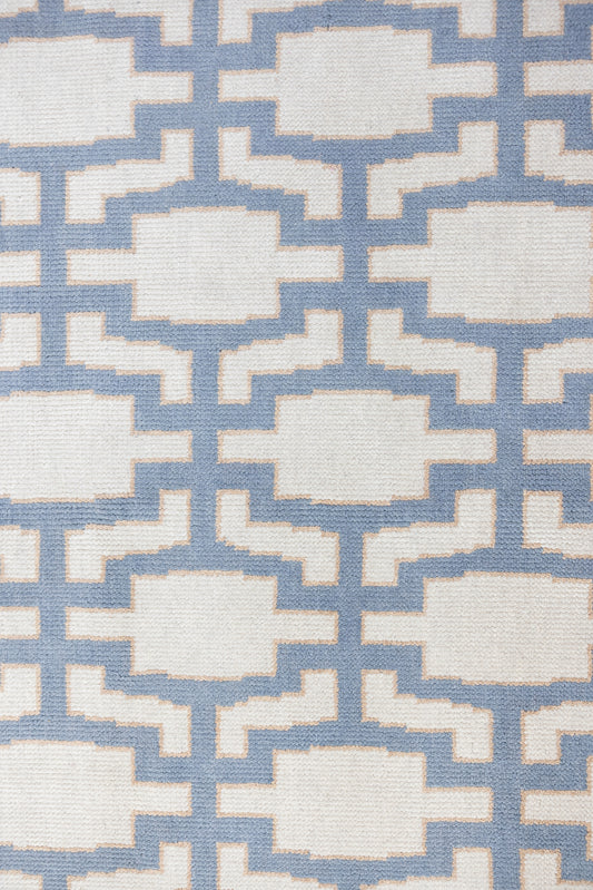 A close-up of a woven rug with a repeating geometric lattice pattern in light blue and off-white.