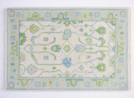 Emogene Mini Rug featuring a vintage-inspired Oushak pattern in soft blue, green, and ivory tones with decorative fringe.