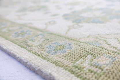 Close-up of Essie hand-knotted wool Oushak rug showing its textured pile and delicate blue and green floral design.