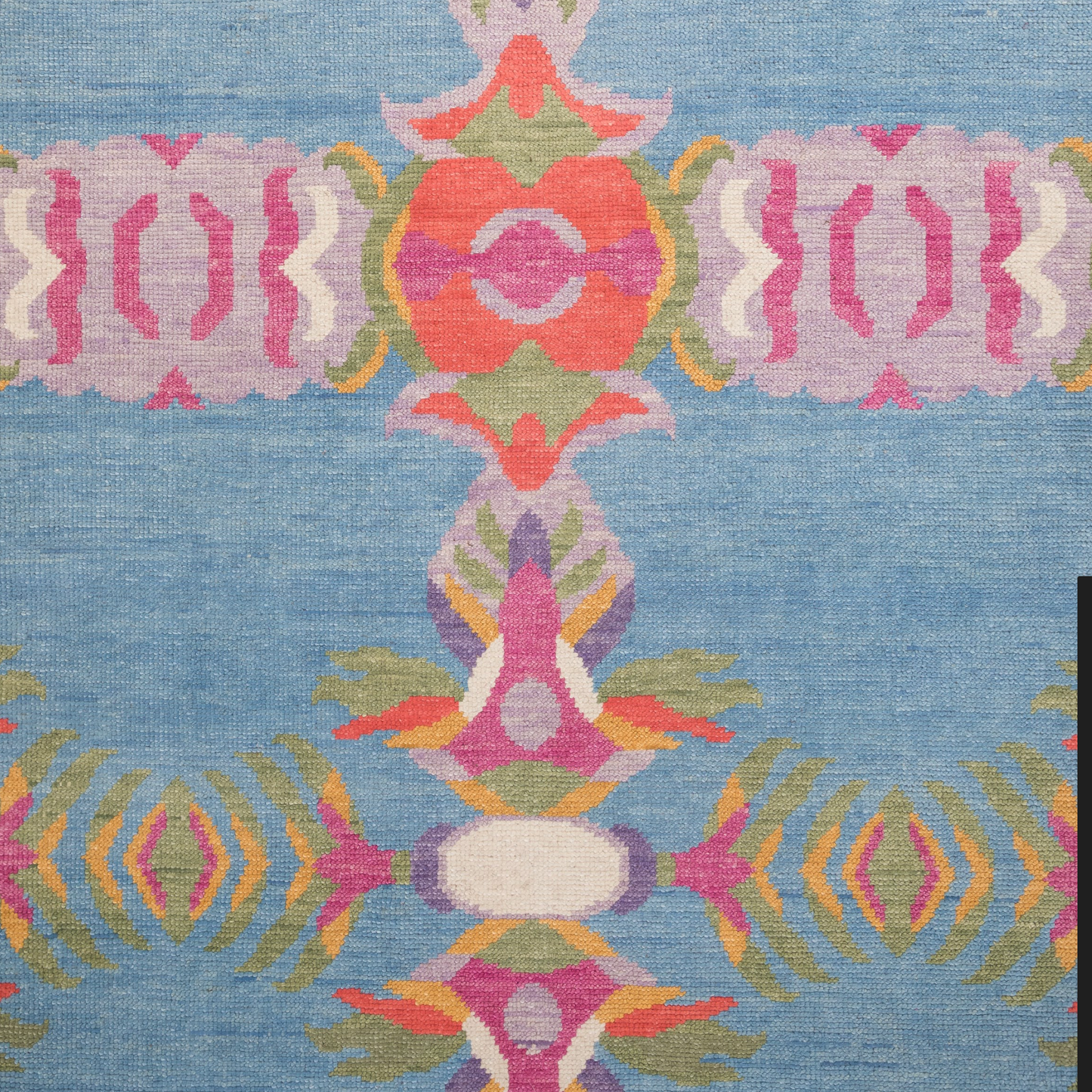 Close-up view of a hand-knotted wool rug with a floral border and medallion layout in punchy colors on a denim blue field.