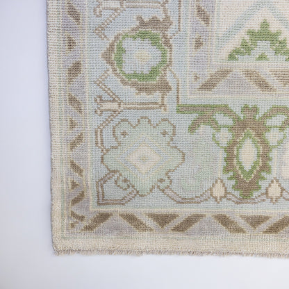 Fern Modern Oushak rug showcasing its decorative geometric border and intricate floral pattern in sage green, pale blue, and ivory.
