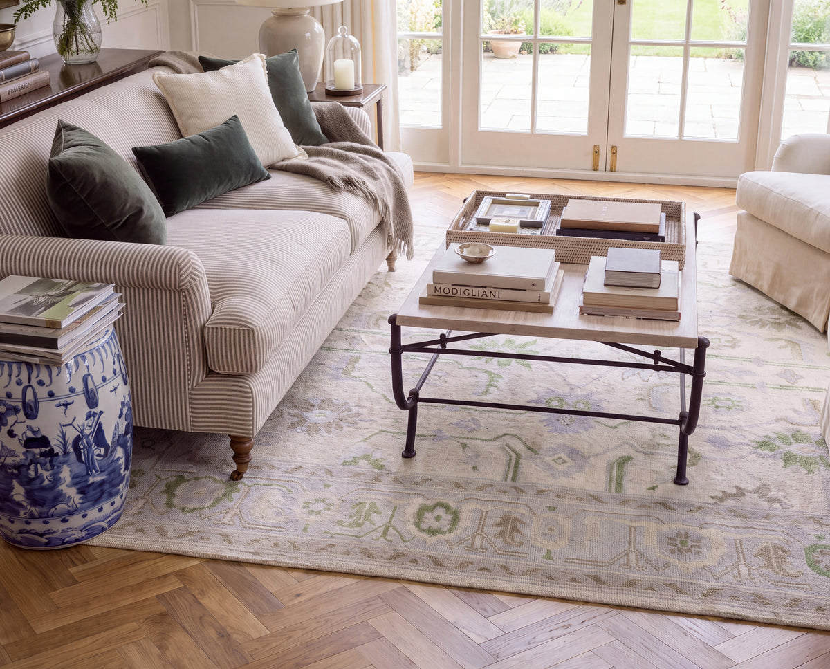 Fern blue and green floral wool Oushak rug beneath a wooden coffee table, featuring delicate botanical motifs and an ivory background.
