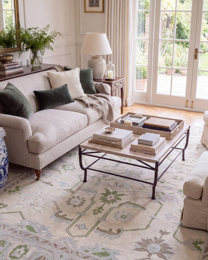Fern hand-knotted floral area rug with soft green vines, powder blue flowers, and lavender accents styled beside a neutral sofa.