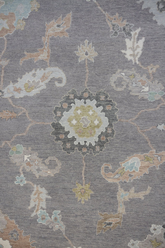 A close-up image of a refined area rug with a floral pattern, featuring deep grey background with subtle purple undertones and intricate motifs in soft pastels, earthy greens, and delicate creams.