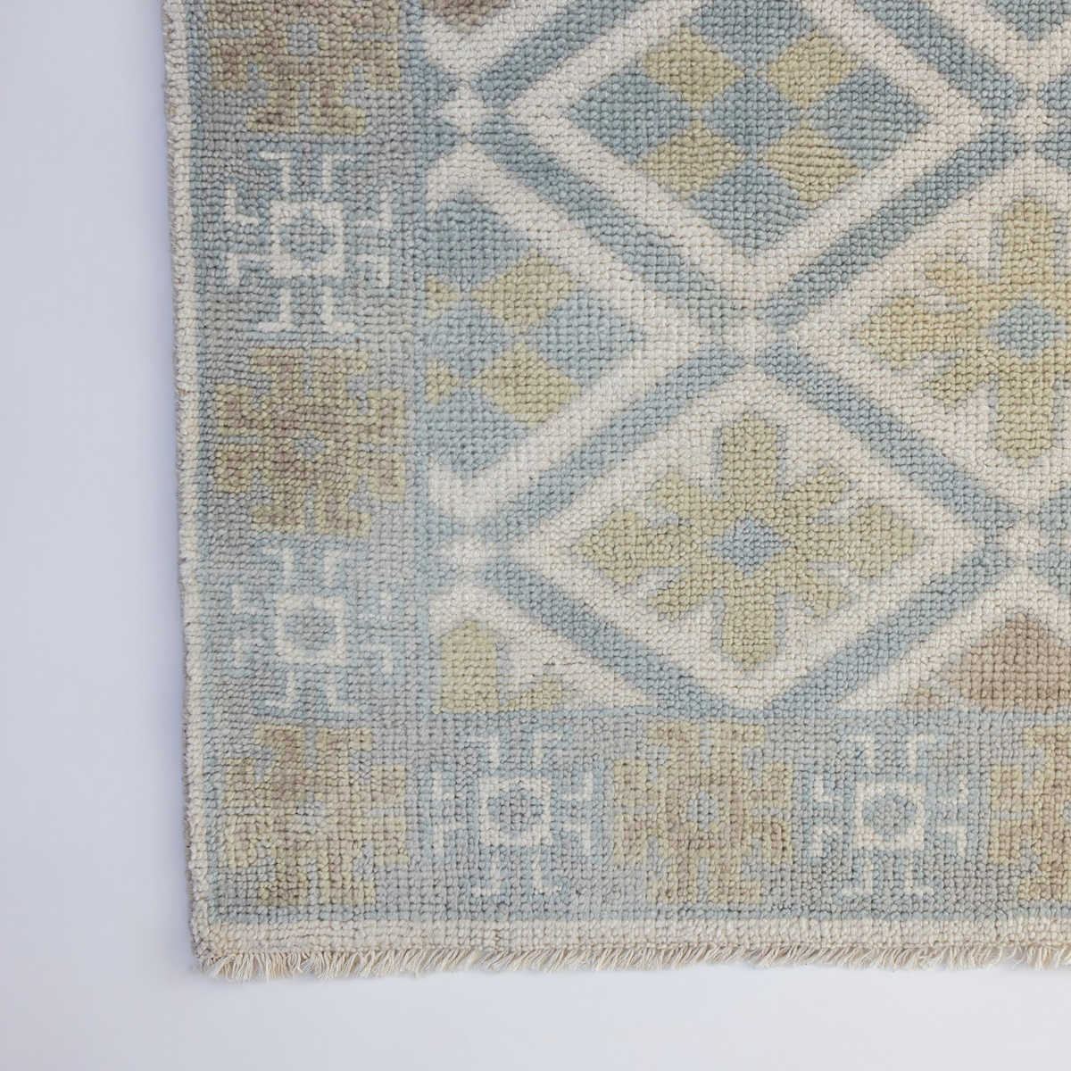 Milly Modern Oushak rug showcasing its decorative border and geometric diamond design in muted blue, sage green, and taupe.