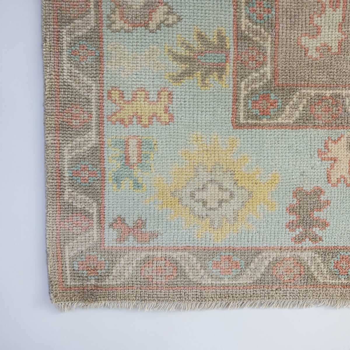 Sookie Modern Oushak rug showcasing its decorative border and colorful botanical motifs in coral pink, turquoise, and buttery yellow.