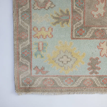 Sookie Modern Oushak rug showcasing its decorative border and colorful botanical motifs in coral pink, turquoise, and buttery yellow.