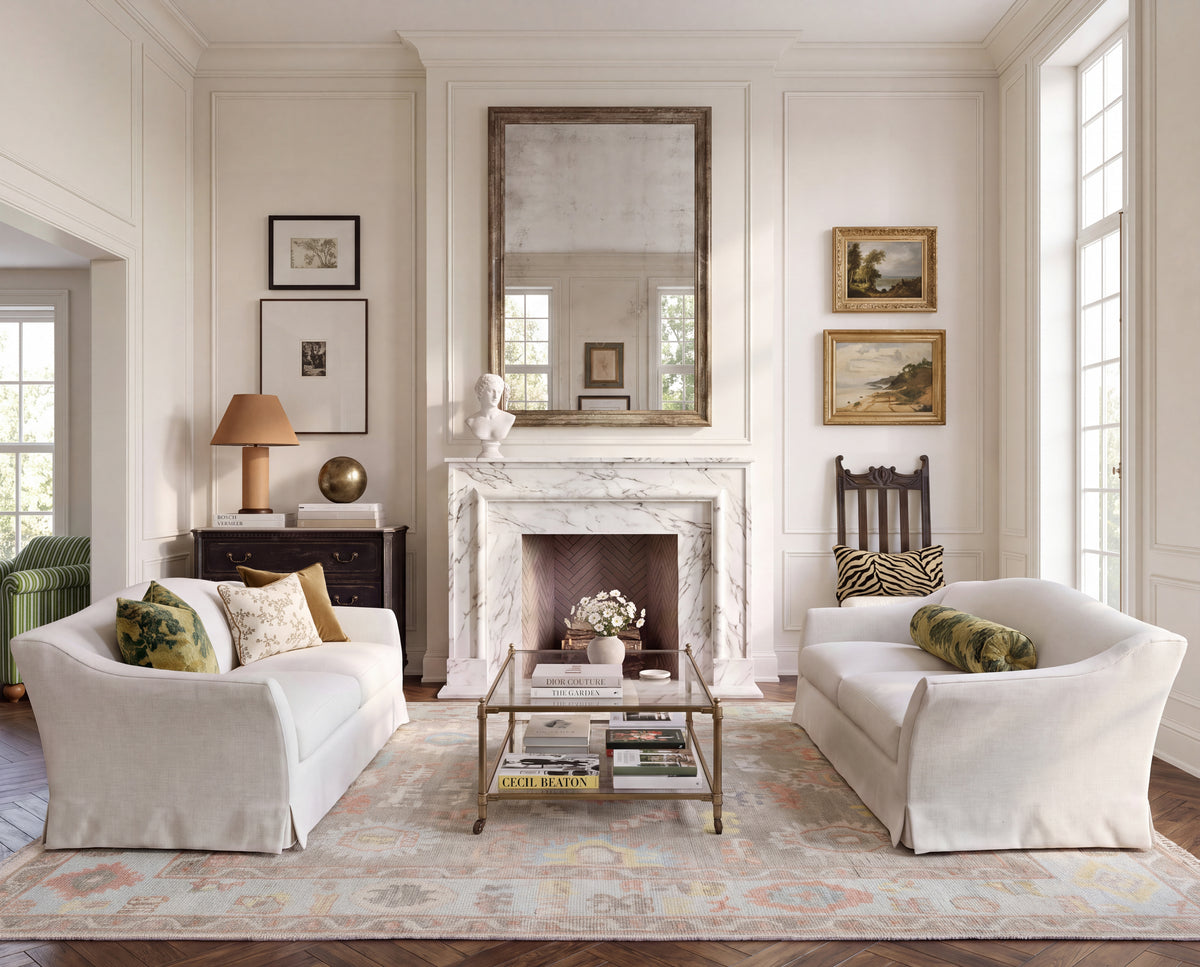 Sookie taupe floral Oushak rug with soft coral, turquoise, and yellow accents styled between cream sofas in an elegant living room.