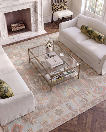 Sookie hand-knotted wool Oushak rug featuring coral pink, turquoise, and yellow floral patterns beneath a glass coffee table.