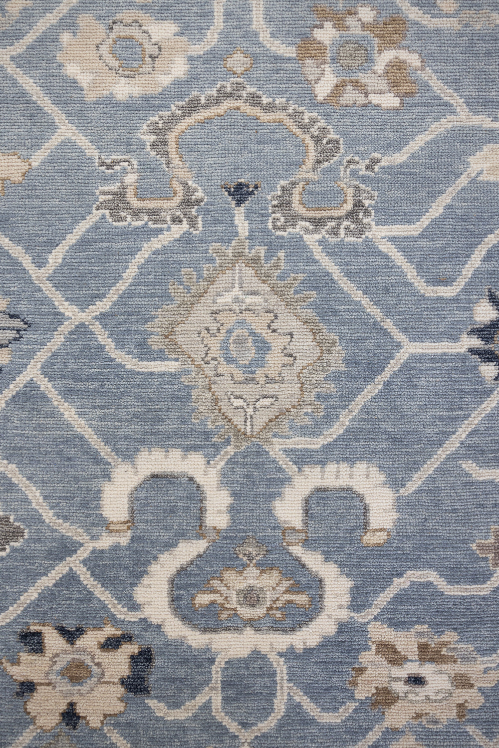 A close-up image of a hand-knotted rug with a floral pattern in a mix of blue and neutral tones.
