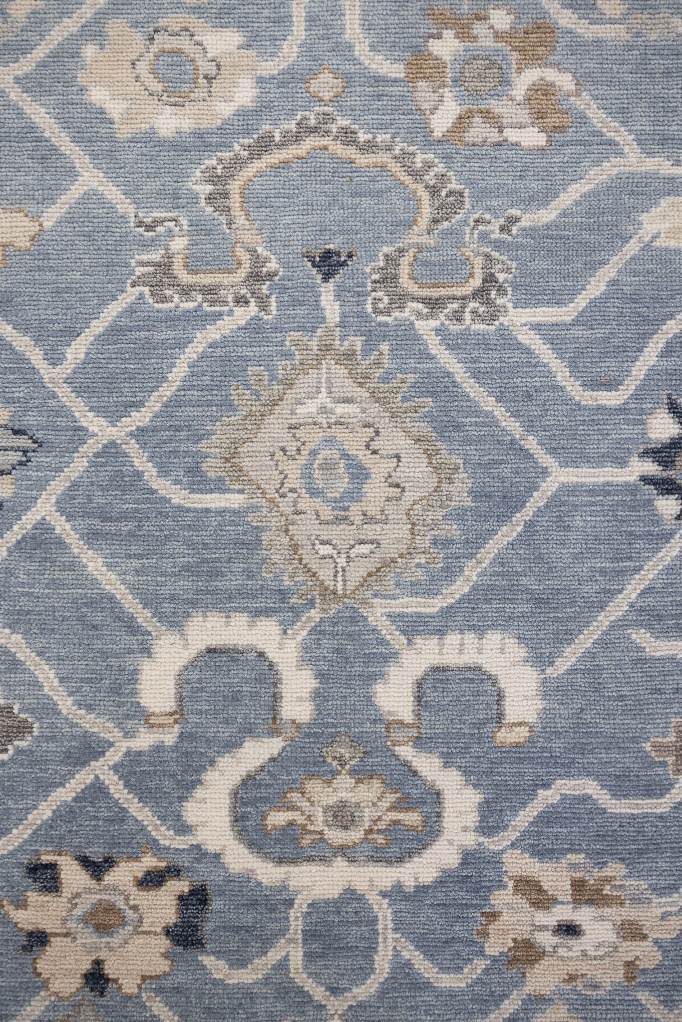 A close-up image of a hand-knotted rug with a floral pattern in a mix of blue and neutral tones.