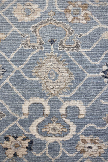 A close-up image of a hand-knotted rug with a floral pattern in a mix of blue and neutral tones.