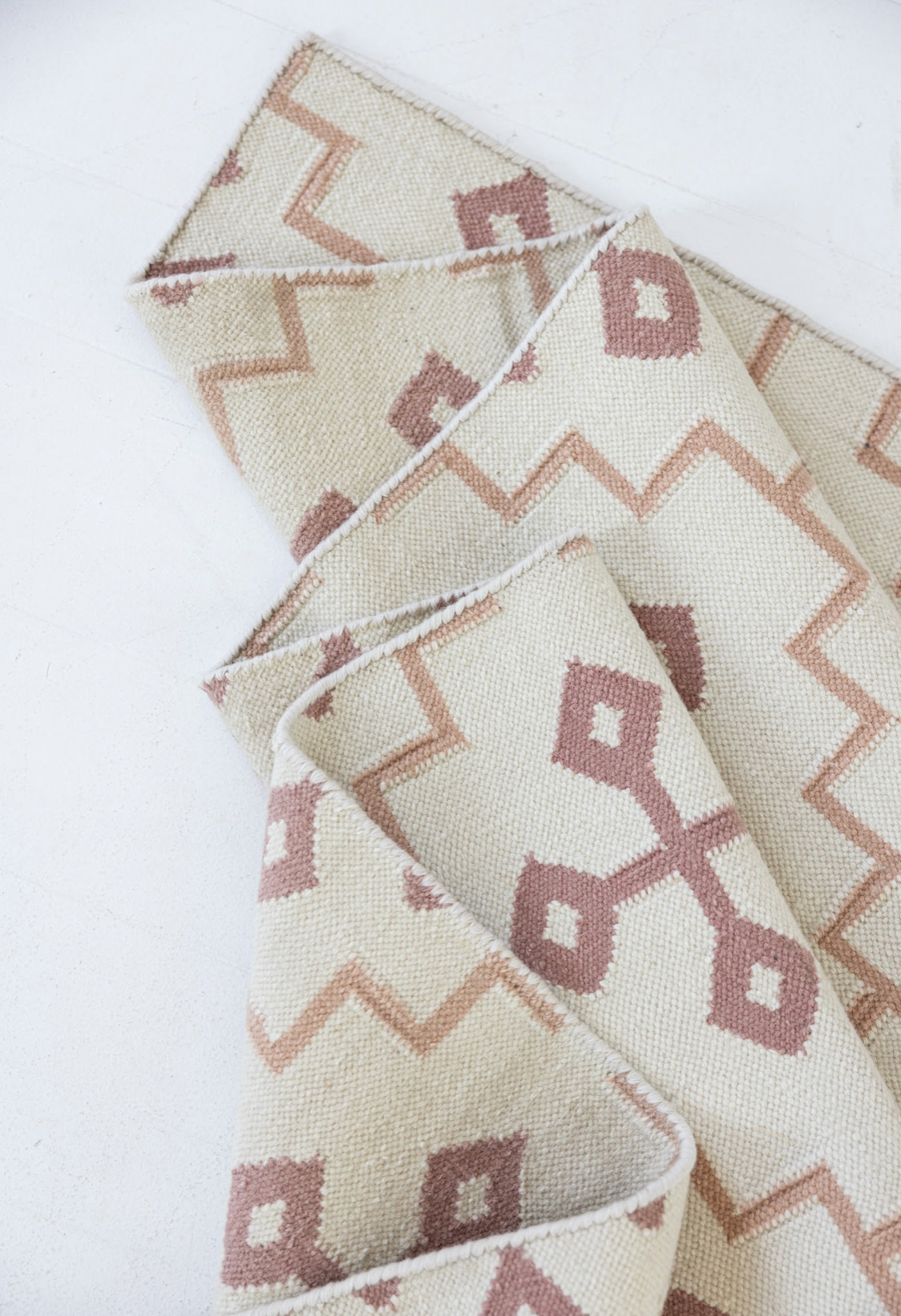 Folded French Rose Flatweave Rug highlighting its handwoven wool texture and reversible construction.