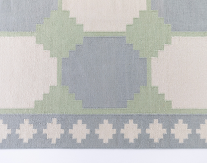 Geometric Flatweave Rug featuring an oversized geometric pattern in soft blue, sage green, and ivory.