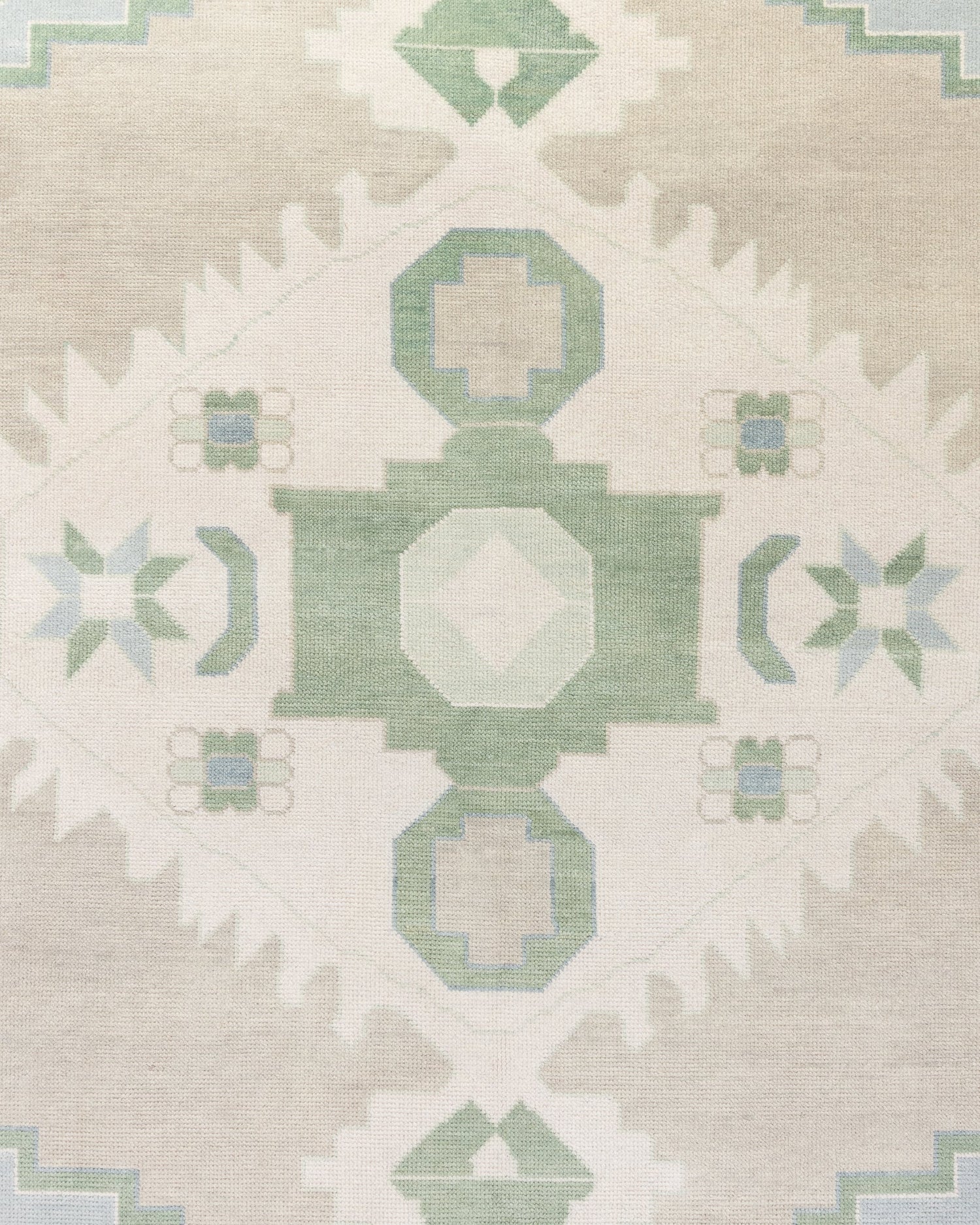 Close-up view of a handcrafted area rug with a geometric medallion pattern and crescent motifs in sage green, soft taupe, and creamy ivory colors.
