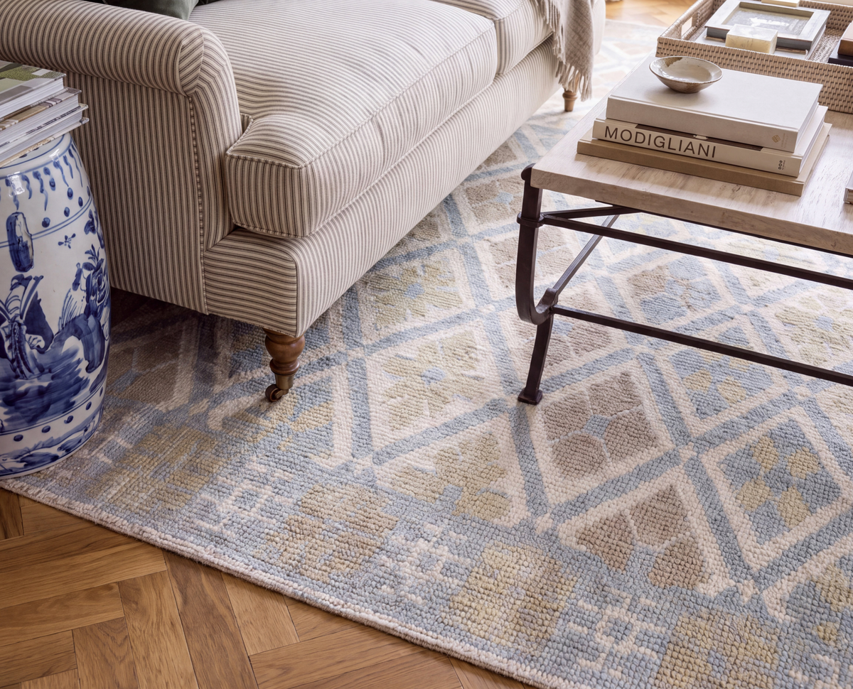 Milly hand-knotted wool rug featuring a soft blue and taupe diamond pattern beneath a cream sofa and wooden coffee table.