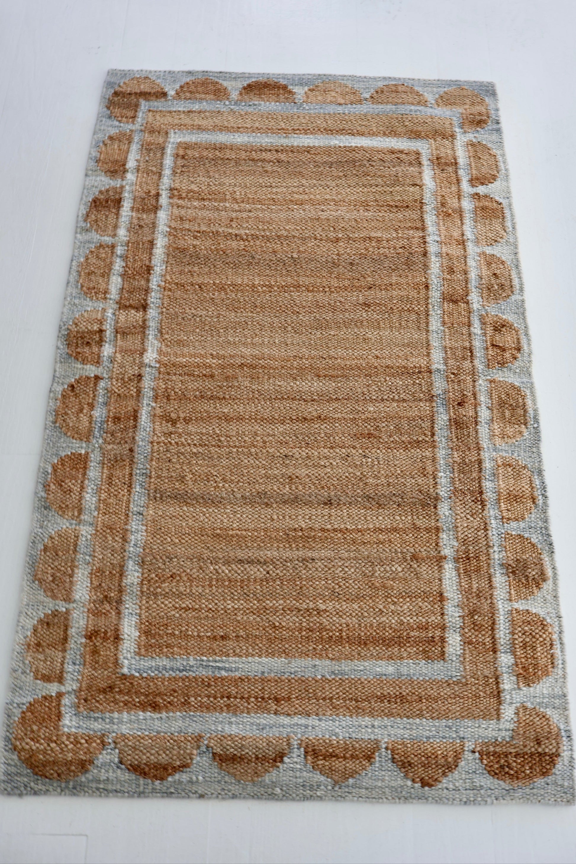 Handwoven jute and wool rug in natural tones with a stone-blue scalloped border – Stone Blue Scalloped Edge Rug by Locust Lane Rugs